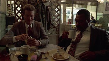 Movie still from “One False Move” (1991), directed by Carl Franklin – Two men sitting at a table with a cup of coffee; Medium shot, Low angle