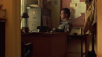 Movie still from “One False Move” (1991), directed by Carl Franklin – A man sitting at a desk in front of a computer; Medium shot, Low angle