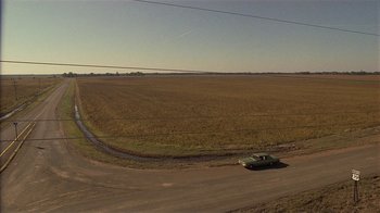 Movie still from “One False Move” (1991), directed by Carl Franklin – A car driving down a dirt road near a field; Extreme Wide shot, High angle