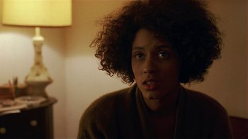 Movie still from “One False Move” (1991), directed by Carl Franklin – A young woman with curly brown hair sitting in a room; Close Up shot, Over the shoulder angle