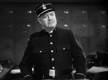 Movie still from “One Hour with You” (1932), directed by George Cukor – A man in a uniform is standing in front of a wall; Medium shot, Low angle