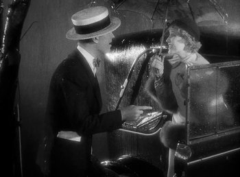 Movie still from “One Hour with You” (1932), directed by George Cukor – A man and a woman in the rain with an open umbrella; Medium shot, High angle