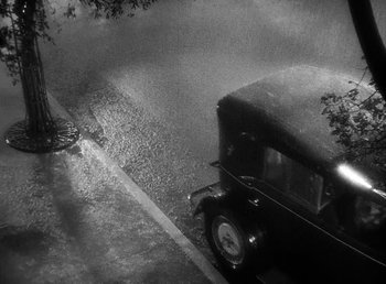 Movie still from “One Hour with You” (1932), directed by George Cukor – An old car parked on the side of the road; Extreme Wide shot, High angle
