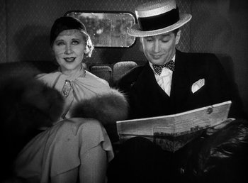 Movie still from “One Hour with You” (1932), directed by George Cukor – A man and a woman sitting in the back of a car reading a newspaper; Medium shot, Low angle