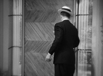 Movie still from “One Hour with You” (1932), directed by George Cukor – A black and white photo of a man in a suit and a hat; Medium shot, High angle