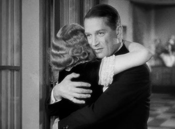 Movie still from “One Hour with You” (1932), directed by George Cukor – A man and a woman hugging each other in front of a window; Medium shot, Over the shoulder angle