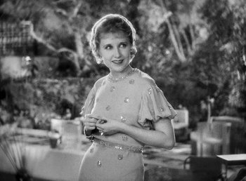 Movie still from “One Hour with You” (1932), directed by George Cukor – An old black and white photo of a woman holding a camera; Medium shot, High angle