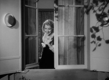Movie still from “One Hour with You” (1932), directed by George Cukor – A black and white photo of a woman standing in front of a door; Medium shot, High angle