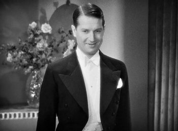 Movie still from “One Hour with You” (1932), directed by George Cukor – A man in a tuxedo standing in front of a flower arrangement; Medium shot, Low angle
