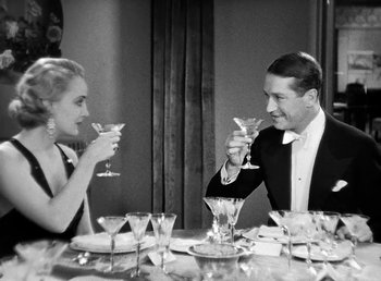 Movie still from “One Hour with You” (1932), directed by George Cukor – A man and a woman sitting at a dinner table drinking champagne; Medium shot, High angle