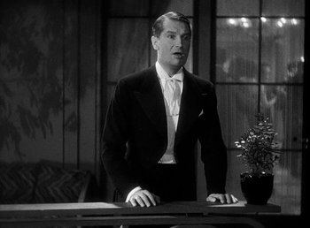 Movie still from “One Hour with You” (1932), directed by George Cukor – A black and white photo of a man standing at a table; Medium shot, Low angle