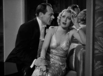 Movie still from “One Hour with You” (1932), directed by George Cukor – A man and a woman sitting next to each other on a couch; Medium shot, High angle