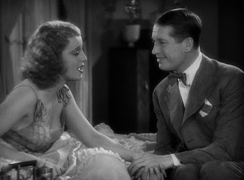 Movie still from “One Hour with You” (1932), directed by George Cukor – A man and a woman sitting on a couch holding hands; Medium shot, High angle