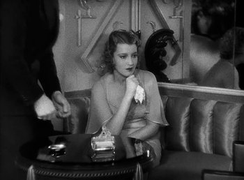 Movie still from “One Hour with You” (1932), directed by George Cukor – A woman sitting at a table in a room; Medium shot, High angle
