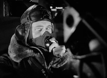 Movie still from “One of Our Aircraft Is Missing” (1942), directed by Emeric Pressburger – A man wearing a helmet and goggles while sitting in an airplane; Medium shot, Low angle