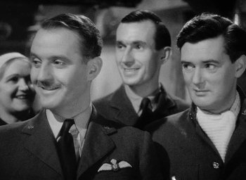 Movie still from “One of Our Aircraft Is Missing” (1942), directed by Emeric Pressburger – A group of three men standing next to each other; Medium shot, Low angle