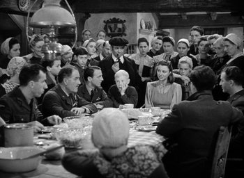 Movie still from “One of Our Aircraft Is Missing” (1942), directed by Emeric Pressburger – A group of people sitting around a table with food; Wide shot, High angle