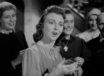 Movie still from “One of Our Aircraft Is Missing” (1942), directed by Emeric Pressburger – An old black and white photo of a woman holding a cell phone; Medium shot, Low angle