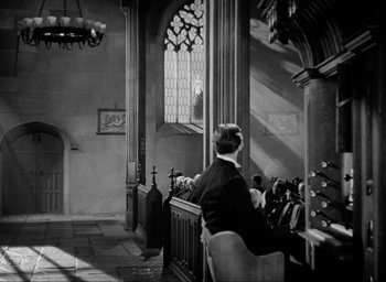 Movie still from “One of Our Aircraft Is Missing” (1942), directed by Emeric Pressburger – A man sitting in a church with a bunch of people sitting around him; Extreme Wide shot, Low angle