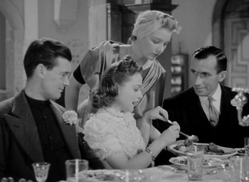 Movie still from “One of Our Aircraft Is Missing” (1942), directed by Emeric Pressburger – An old black and white photo of a woman and two men at a dinner table; Medium shot, Over the shoulder angle
