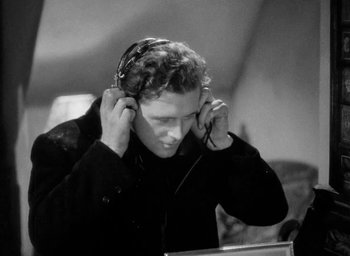Movie still from “One of Our Aircraft Is Missing” (1942), directed by Emeric Pressburger – A black and white photo of a man listening to headphones; Close Up shot, Low angle