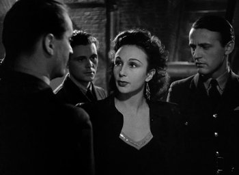 Movie still from “One of Our Aircraft Is Missing” (1942), directed by Emeric Pressburger – A group of men and a woman standing next to each other; Medium shot, Over the shoulder angle