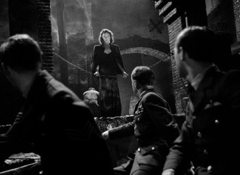 Movie still from “One of Our Aircraft Is Missing” (1942), directed by Emeric Pressburger – A woman standing in front of a group of soldiers; Wide shot, Low angle