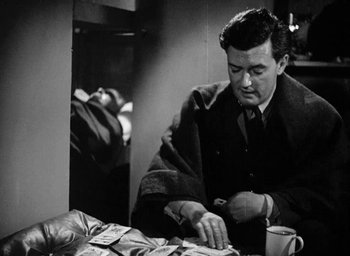 Movie still from “One of Our Aircraft Is Missing” (1942), directed by Emeric Pressburger – A black and white photo of a man cutting money; Medium shot, Over the shoulder angle