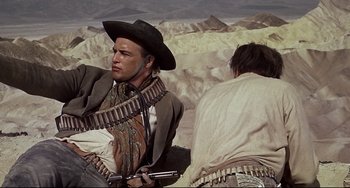 Movie still from “One-Eyed Jacks” (1961), directed by Marlon Brando – A man with a gun sitting next to another man in the desert; Medium shot, Low angle