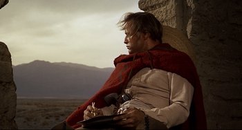 Movie still from “One-Eyed Jacks” (1961), directed by Marlon Brando – A man sitting in a chair with a red blanket on his shoulders; Medium shot, Low angle