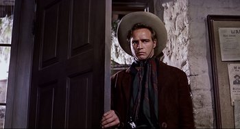 Movie still from “One-Eyed Jacks” (1961), directed by Marlon Brando – A man holding a sword in front of a door; Medium shot, Low angle