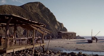 Movie still from “One-Eyed Jacks” (1961), directed by Marlon Brando – People sitting at tables on a beach near a mountain; Extreme Wide shot, High angle
