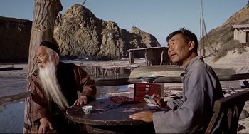 Movie still from “One-Eyed Jacks” (1961), directed by Marlon Brando – Two men sitting at a table in front of a mountain; Medium shot, Low angle