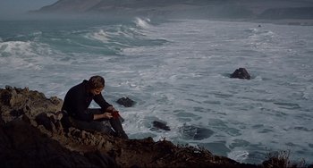 Movie still from “One-Eyed Jacks” (1961), directed by Marlon Brando – A man sitting on a rock near the ocean; Wide shot, High angle