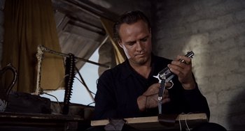 Movie still from “One-Eyed Jacks” (1961), directed by Marlon Brando – A man in a black shirt is working on a gun; Close Up shot, Low angle