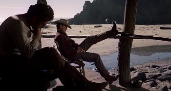 Movie still from “One-Eyed Jacks” (1961), directed by Marlon Brando – A man in a cowboy hat sitting in a chair on the beach; Wide shot, Low angle