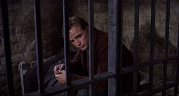 Movie still from “One-Eyed Jacks” (1961), directed by Marlon Brando – A man sitting on the ground next to a jail cell; Close Up shot, High angle