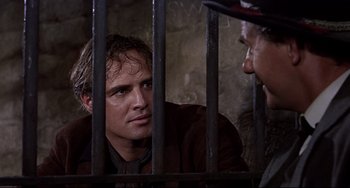 Movie still from “One-Eyed Jacks” (1961), directed by Marlon Brando – A man sitting in front of another man behind bars; Close Up shot, Over the shoulder angle
