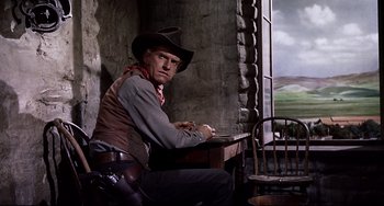 Movie still from “One-Eyed Jacks” (1961), directed by Marlon Brando – A man sitting at a table wearing a cowboy hat; Medium shot, Low angle
