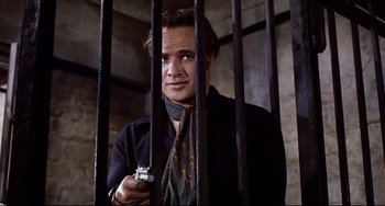Movie still from “One-Eyed Jacks” (1961), directed by Marlon Brando – A man holding a cell phone behind a fence; Close Up shot, Low angle