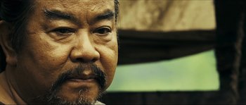 Movie still from “Ong Bak 2” (2008), directed by Tony Jaa – An older man with a beard and mustache; Close Up shot, Low angle