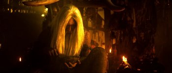 Movie still from “Ong Bak 2” (2008), directed by Tony Jaa – A man with long blonde hair sitting next to a fire; Medium shot, Low angle