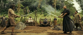 Movie still from “Ong Bak 2” (2008), directed by Tony Jaa – A group of people sitting on a bench in the woods; Wide shot, Low angle