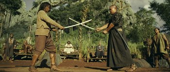 Movie still from “Ong Bak 2” (2008), directed by Tony Jaa – Two men are holding swords in the middle of an outdoor scene; Wide shot, Low angle