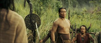 Movie still from “Ong Bak 2” (2008), directed by Tony Jaa – A man holding a sword in a grassy area; Medium shot, Low angle