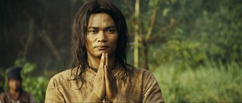 Movie still from “Ong Bak 2” (2008), directed by Tony Jaa – A man with long black hair is holding his hands in prayer; Close Up shot, Low angle