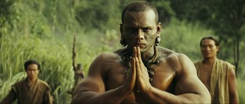 Movie still from “Ong Bak 2” (2008), directed by Tony Jaa – A man with tattoos on his face is praying in the woods; Close Up shot, Low angle