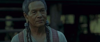 Movie still from “Ong Bak 2” (2008), directed by Tony Jaa – An older man wearing a long necklace and wearing a large earring; Close Up shot, Over the shoulder angle