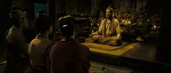 Movie still from “Ong Bak 2” (2008), directed by Tony Jaa – A man sitting on a mat in front of a woman; Wide shot, Over the shoulder angle