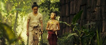 Movie still from “Ong Bak 2” (2008), directed by Tony Jaa – A woman standing next to a young girl holding a stick; Medium shot, Over the shoulder angle